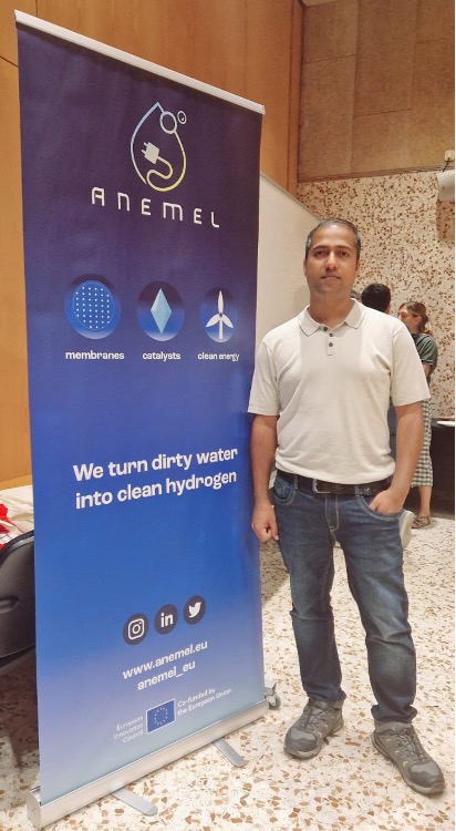 A picture of ANEMEL researcher Suraj Gupta near a rollup banner of the project